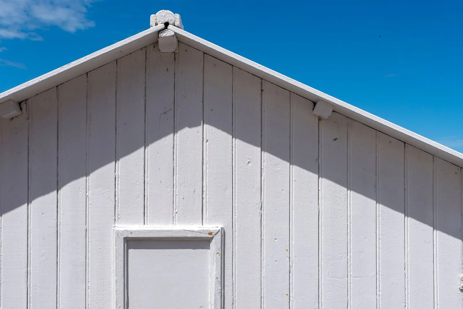 White painted board and batten siding on a house gable, wide vertical boards with narrow battens over the seams, under a blue sky