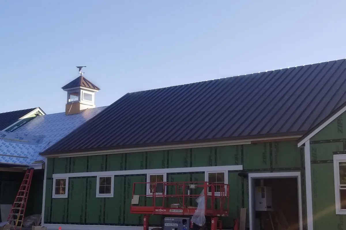 Dark standing-seam metal panels installed on a new building, with white roof underlayment still exposed on the roof section beside it