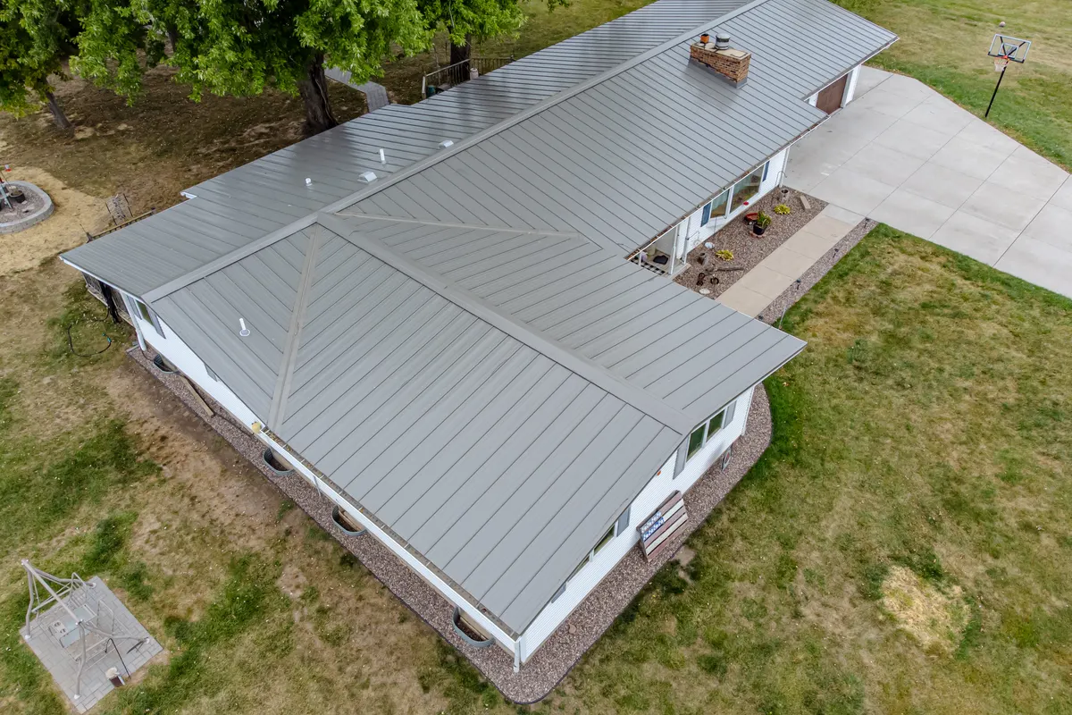 Aerial view of a one-story house with a light gray low-slope standing-seam metal roof