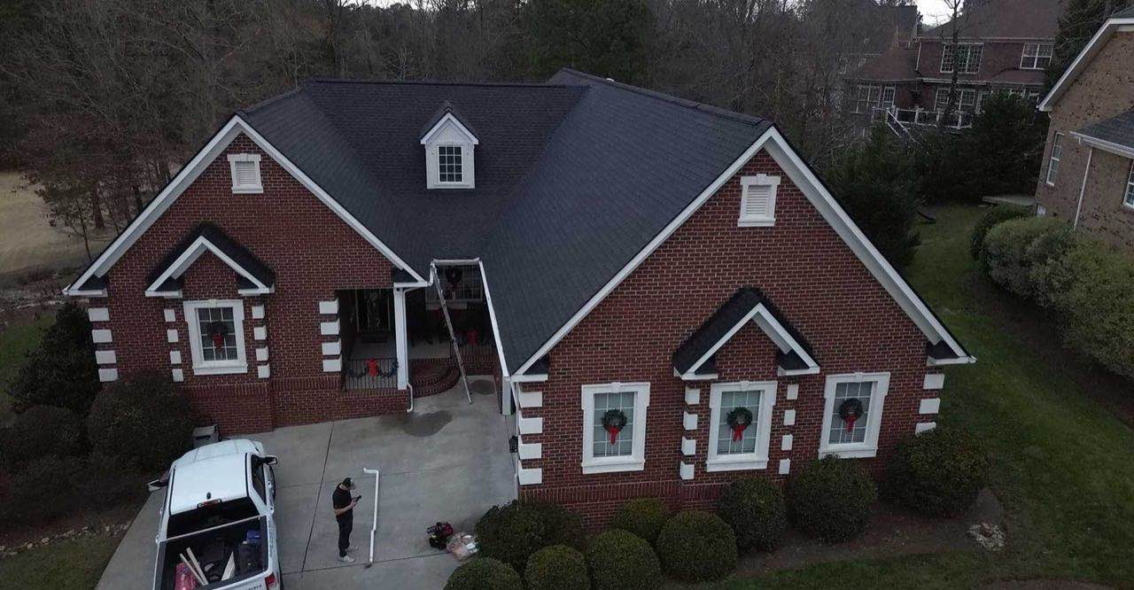 Drone view of a brick house with a hip-and-gable shingle roof in the Myrtle Beach area, inspector standing in the driveway