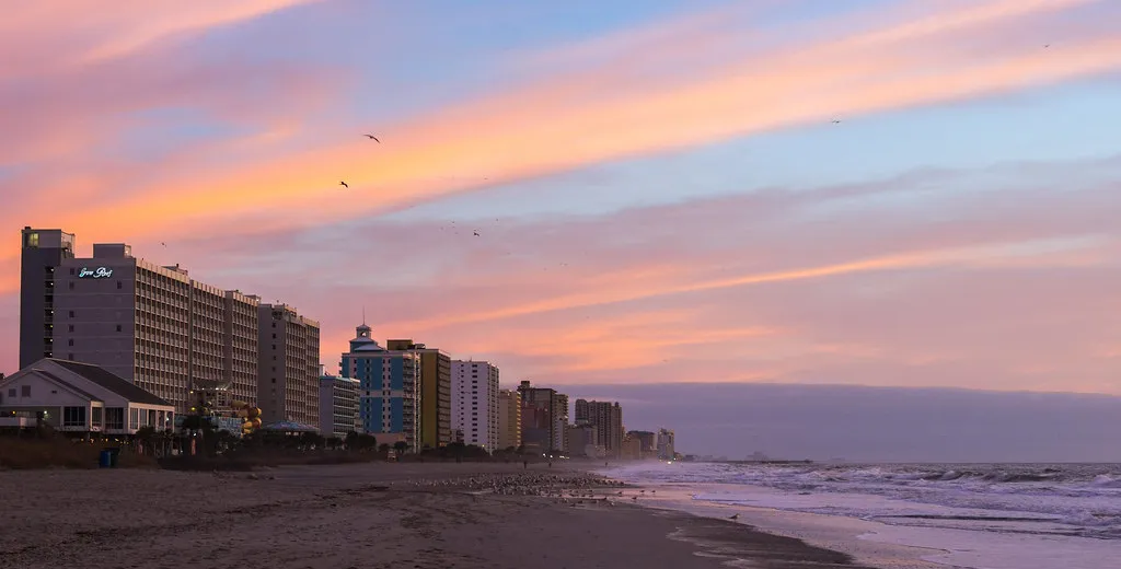 Row of oceanfront hotel and condo towers along the beach in Myrtle Beach at sunrise, with waves on the right