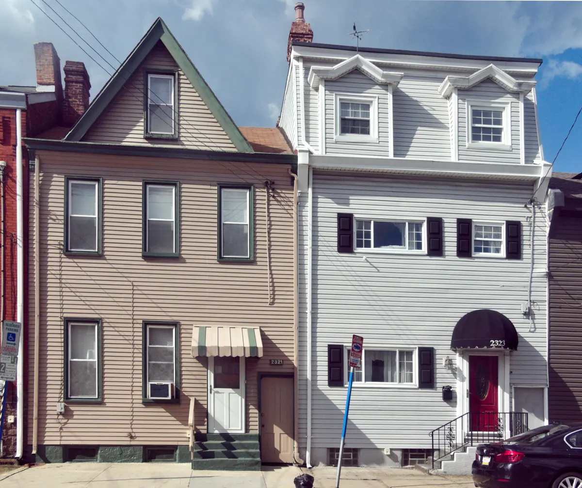 Two row houses with horizontal vinyl lap siding, one tan and one light gray, with shutters and an awning