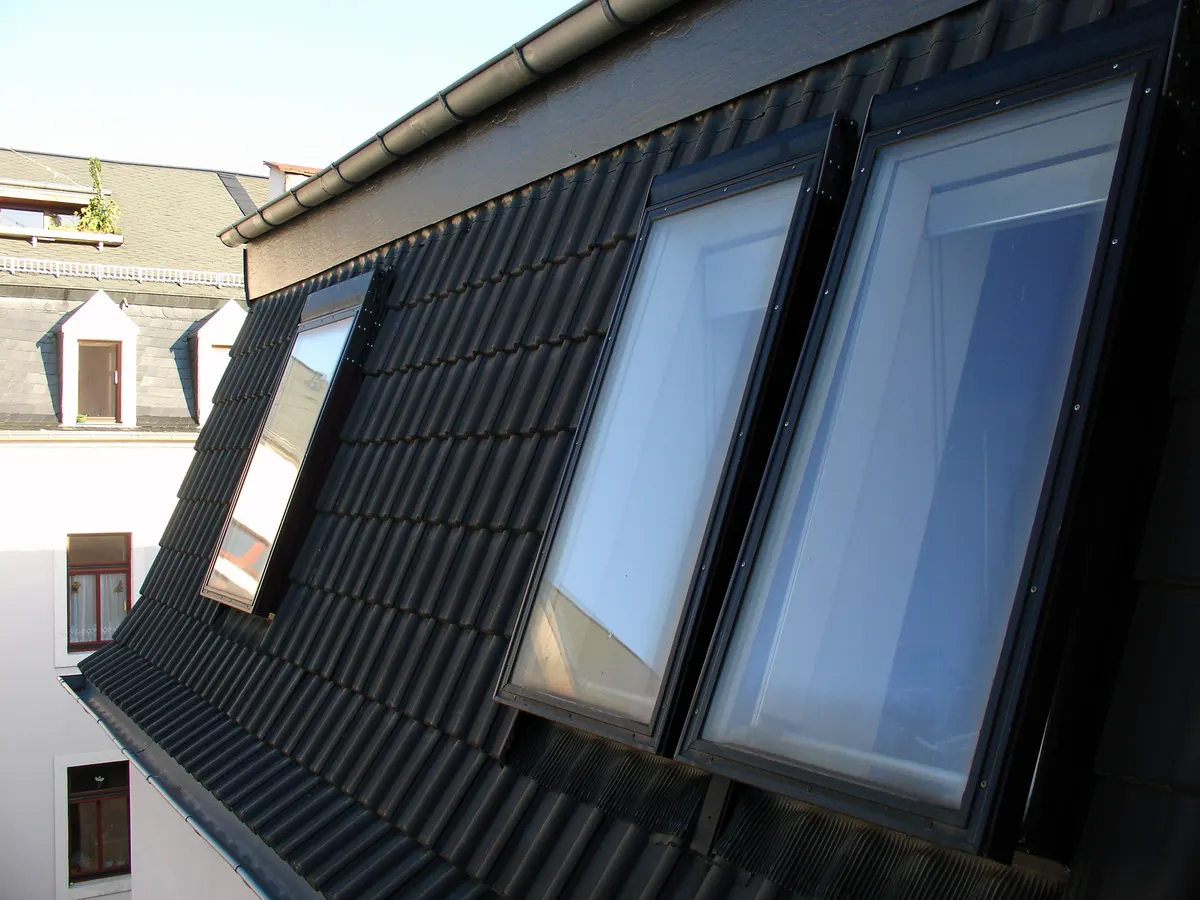 Three glass roof-window skylights set into a dark tile roof, each with its own flashing frame