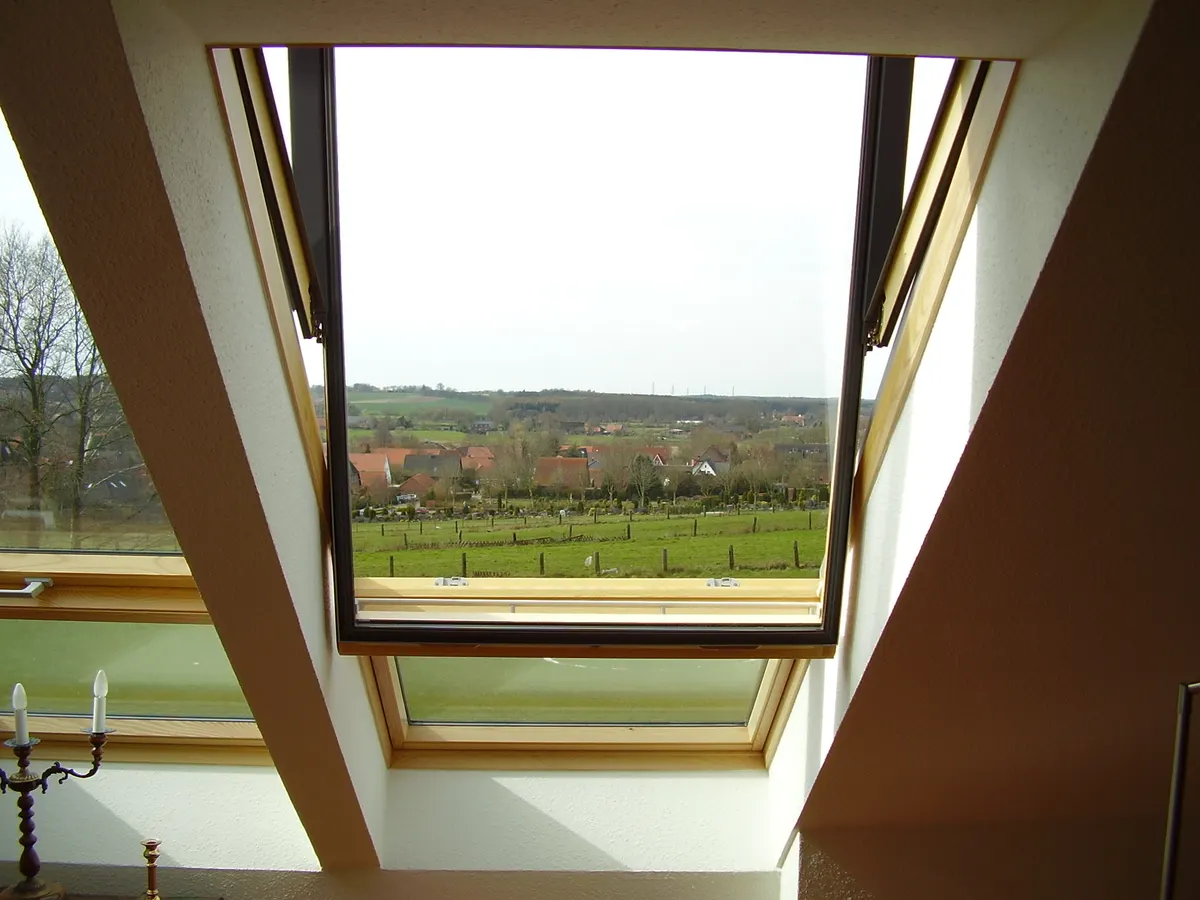 Venting skylight swung open in a sloped ceiling, seen from inside the room, with daylight and the view beyond